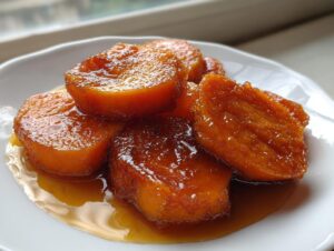 Close-up of thick slices of bright orange candied yams coated in a thick, glossy brown sugar glaze.