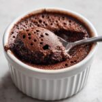 A spoonful of airy, dark chocolate mousse being lifted from a white ramekin.