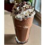 A tall glass filled with blended frozen hot chocolate, topped with whipped cream and chocolate shavings.