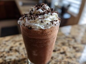A tall glass filled with blended frozen hot chocolate, topped with whipped cream and chocolate shavings.