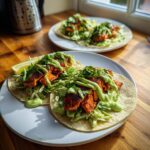 Two perfectly assembled salmon tacos topped with slaw, cilantro, and a bright green creamy sauce.