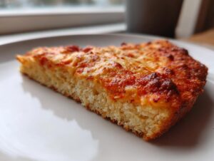 Close-up of a thick slice of keto pizza crust topped with melted, slightly browned cheese.