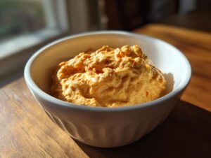 Close-up of a creamy, orange-colored beer cheese dip served in a white bowl on a wooden surface.