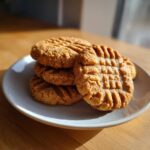 A stack of freshly baked peanut butter cookies featuring the classic criss-cross fork pattern, resting on a small white plate.