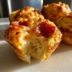 A close-up of one of the amazing pizza muffins with a bite taken out, showing melted cheese and pepperoni on top.