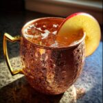 Close-up of a frosty copper mug filled with an apple cider Moscow mule, garnished with a fresh apple slice.