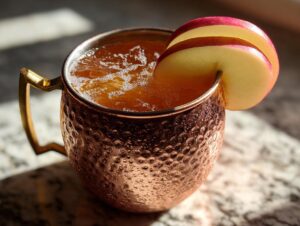 Close-up of a frosty apple cider moscow mule in a hammered copper mug, garnished with thin apple slices.
