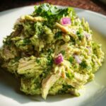 A close-up serving of creamy avocado chicken salad mixed with shredded chicken, cilantro, and diced red onion.