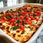 Close-up of a baked, cheesy bruschetta dip topped generously with diced fresh tomatoes and basil.