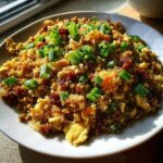 A close-up shot of savory cauliflower fried rice mixed with scrambled egg and topped generously with bright green chopped scallions.