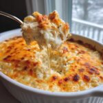 A spoonful of creamy, cheesy chicken and rice casserole lifted from a white baking dish, showing melted cheese strings.