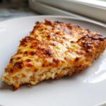 A close-up of a cheesy slice of keto pizza crust with a golden-brown, bubbly top.