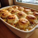 Close-up of a baked chicken pot pie casserole topped with golden, fluffy biscuits nestled in creamy filling.