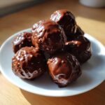 A stack of rich, chocolate-glazed pecan pie balls piled high on a small white plate.