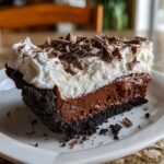 A rich slice of Christmas chocolate cream pie featuring a dark crust, thick chocolate filling, and whipped cream topped with chocolate shavings.
