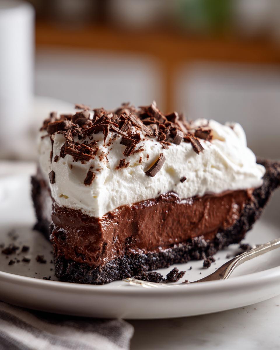 A decadent slice of Christmas chocolate cream pie featuring a dark crust, rich chocolate filling, and whipped topping with chocolate shavings.