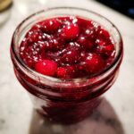 Close-up of a glass jar filled with vibrant, chunky cranberry christmas jam, showing whole berries.