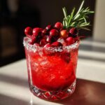 A festive cranberry pomegranate margarita in a sugared glass, topped with fresh cranberries and rosemary.