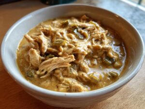 Close-up of a white bowl filled with creamy, shredded cream cheese chicken chili and green chiles.