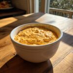 A creamy, orange-colored beer cheese dip served warm in a white bowl on a wooden table.