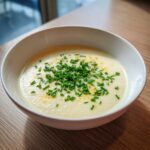 A bowl of creamy, pale yellow cauliflower soup topped generously with bright green chopped chives.