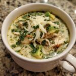Close-up of creamy chicken poblano soup recipe, featuring shredded chicken, avocado chunks, and shredded cheese.