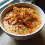 Close-up of a white bowl filled with creamy chicken tortilla soup, topped generously with crispy fried tortilla strips.