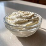 A small glass bowl filled with thick, creamy homemade garlic sauce, topped with cracked black pepper.