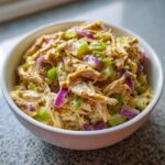 A close-up of creamy honey mustard chicken salad mixed with diced red onion and celery in a white bowl.