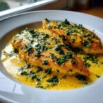 Two pan-seared chicken breasts smothered in a rich, yellow creamy lemon chicken sauce and topped with fresh parsley.