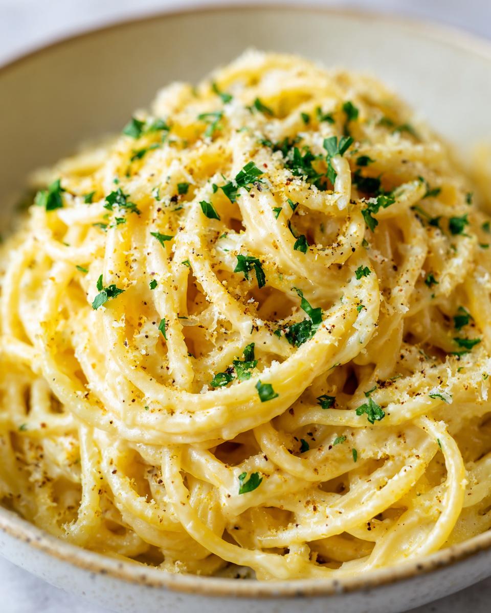 A close-up shot of a bowl filled with rich, creamy lemon pasta, topped with grated cheese and fresh parsley.
