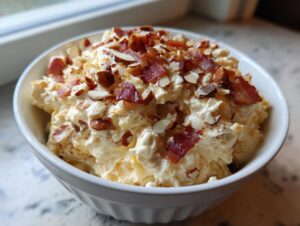 A close-up of creamy Neiman Marcus dip served in a white bowl, generously topped with crumbled bacon and sliced almonds.
