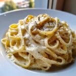 Close-up of fettuccine pasta generously coated in rich homemade alfredo sauce and sprinkled with black pepper.