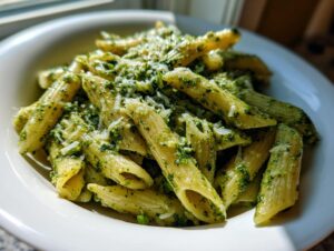 Close-up of penne pasta coated in vibrant green sauce, served as creamy pesto pasta and topped with grated cheese.