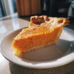 A close-up, sunlit slice of creamy sweet potato pie resting on a white plate.