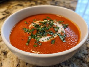 A close-up of a bowl of rich, red tomato bisque, swirled with cream and topped with fresh chopped basil.