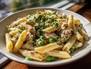 Close-up of creamy tuna pasta featuring penne, flaked tuna, green peas, and parsley garnish.