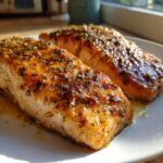 Two perfectly cooked, glazed, and seasoned fillets of air fryer salmon resting on a white plate.