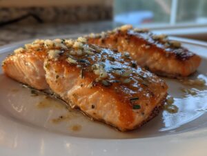 Two perfectly cooked fillets of air fryer salmon topped with a glistening garlic and herb glaze on a white plate.