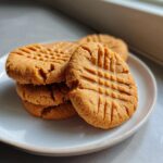 A small stack of golden brown Easy Peanut Butter Cookies showing classic crosshatch fork marks on a light plate.