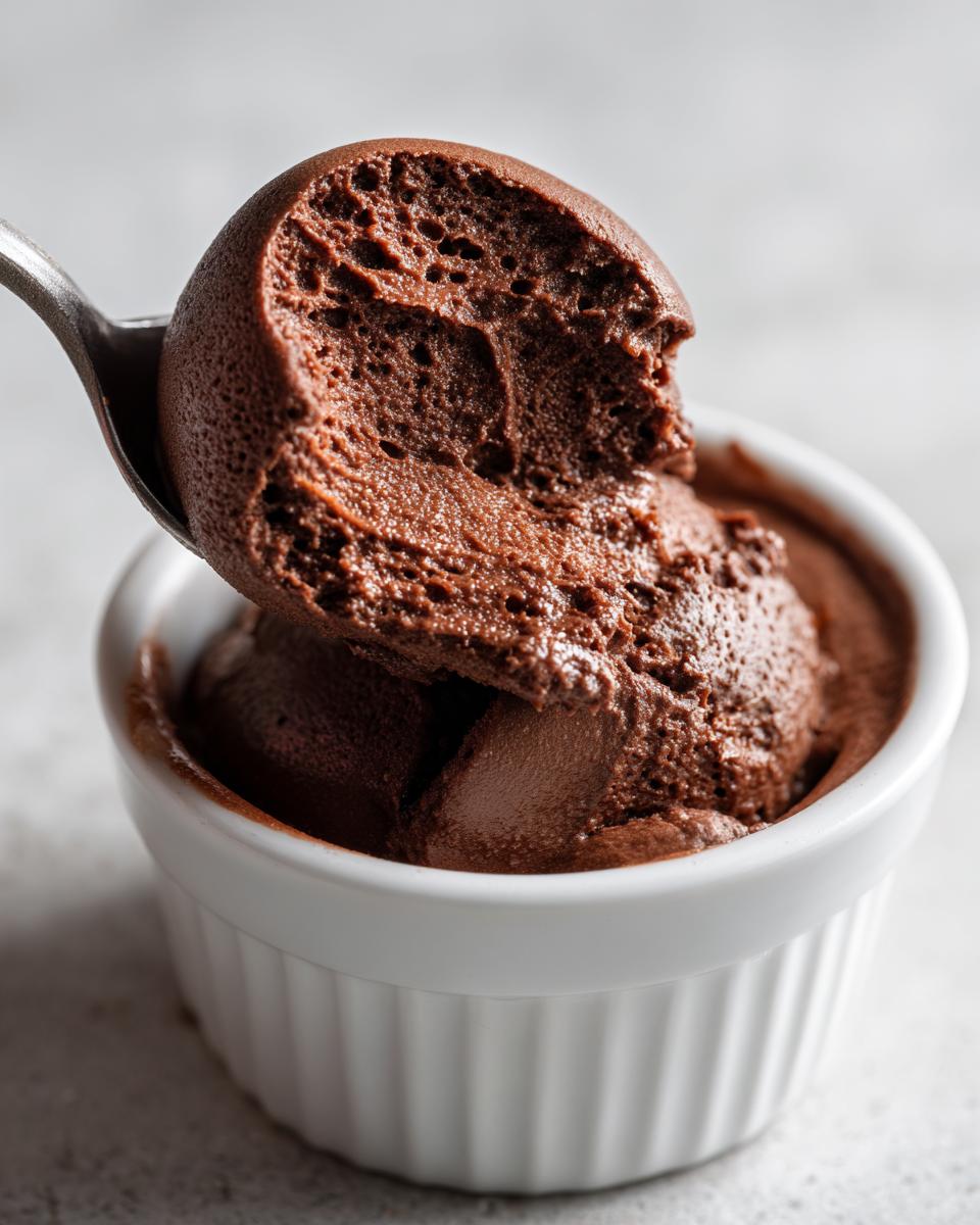 A spoonful of airy, dark chocolate mousse being lifted from a white ramekin.