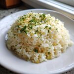 A mound of fluffy white garlic butter rice garnished with chopped fresh parsley and seasoning.
