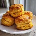 A stack of four fluffy, golden-orange sweet potato biscuits drizzled with a light glaze, sitting on a white plate.