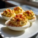 Four creamy deviled eggs topped with paprika, ready to serve on a white plate.