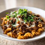 A close-up of french onion pasta featuring fusilli noodles topped with rich caramelized onions, melted cheese, and fresh parsley.