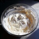 Close-up of thick, bright white, freshly mixed royal icing recipe peaks in a clear glass bowl.