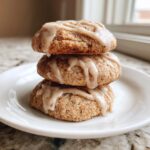 Three soft, round applesauce cookies stacked and drizzled with a light brown spice glaze.