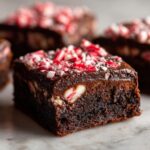 A close-up of a fudgy square of candy cane brownies, topped with chocolate glaze and crushed peppermint candy.