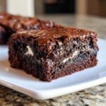 Close-up of a fudgy Oreo brownie square showing a shiny top and a creamy white filling layer.