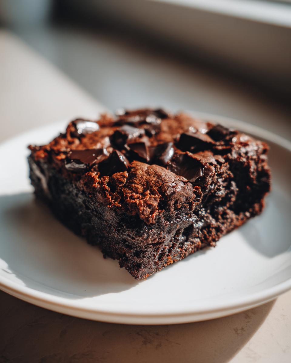 A close-up, richly colored slice of fudgy sweet potato brownies topped with melted chocolate chunks on a white plate.